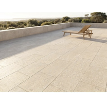 Moderne Terrasse mit großen Steinplatten, einer Holzsonnenliege und einer Steinmauer mit Blick auf eine Landschaft und das Meer.