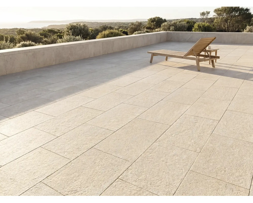 Moderne Terrasse mit großen Steinplatten, einer Holzsonnenliege und einer Steinmauer mit Blick auf eine Landschaft und das Meer.