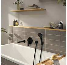 Baignoire moderne avec robinetterie encastrée noir mat, carrelage gris et étagères en bois avec accessoires de salle de bain.