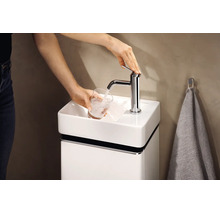 Eine Person füllt ein Glas mit Wasser aus einer verchromten Armatur an einem kleinen weißen Gäste-Waschbecken mit passendem Unterschrank.