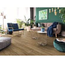Salon moderne avec sol aspect bois, canapé marron, fauteuil bleu, tables d'appoint dorées et mur vert avec plantes d'intérieur.