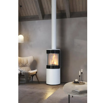 Moderner, runder Kaminofen in Weiß mit brennendem Feuer im Wohnzimmer neben einem Sessel und einem Tisch.