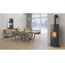 Moderner Wohn- und Essbereich mit einem brennenden schwarzen Kaminofen, einem großen Holztisch mit Polsterstühlen und hellem Ambiente.