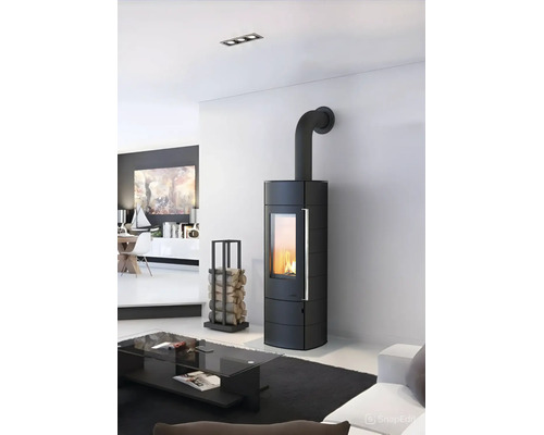 Moderner schwarzer Kaminofen mit großem Sichtfenster und brennendem Feuer in einem hellen Wohnzimmer neben einem Kaminholzregal.
