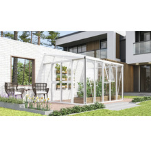 Serre adossée blanche en aluminium et verre contre un mur en briques blanches sur une terrasse moderne avec plantes et meubles de jardin.