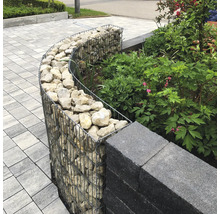 Gabion courbe rempli de pierres pour bordure de jardin pres du mur et des plantes sur un sol pave.