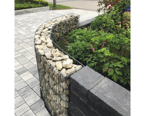 Gabion courbe rempli de pierres pour bordure de jardin pres du mur et des plantes sur un sol pave.