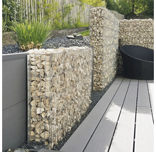 Mur en gabion avec paniers métalliques remplis de pierres claires sur une terrasse avec des lames grises dans un jardin.