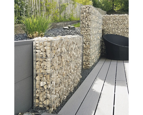 Mur en gabion avec paniers métalliques remplis de pierres claires sur une terrasse avec des lames grises dans un jardin.
