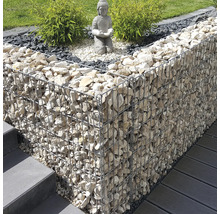 Aménagement de jardin moderne avec mur en gabion, statue de Bouddha sur gravier et plantes vertes près d'un escalier et d'une terrasse.