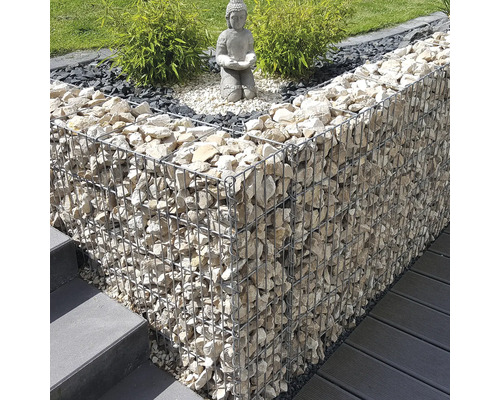 Aménagement de jardin moderne avec mur en gabion, statue de Bouddha sur gravier et plantes vertes près d'un escalier et d'une terrasse.