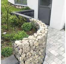 Gabion courbe comme bordure de jardin, rempli de pierres naturelles claires à côté d'un chemin pavé.