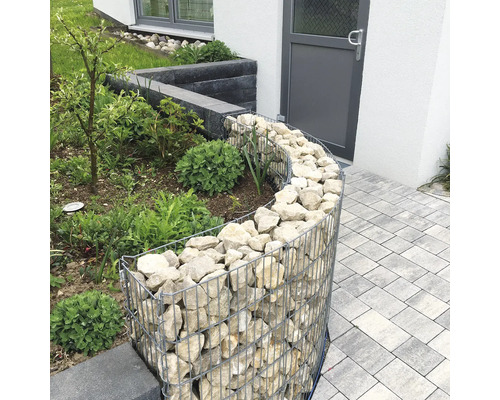 Gabion courbe comme bordure de jardin, rempli de pierres naturelles claires à côté d'un chemin pavé.