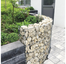 Gabion courbé en treillis métallique rempli de pierres naturelles servant de bordure de parterre dans un jardin.