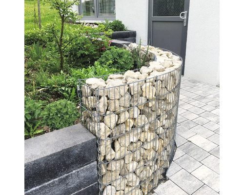 Gabion courbé en treillis métallique rempli de pierres naturelles servant de bordure de parterre dans un jardin.