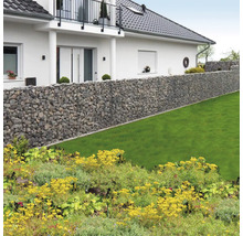 Long mur de gabions en pierre naturelle dans un jardin lumineux avec pelouse devant une maison avec balcon.