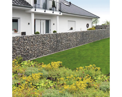 Long mur de gabions en pierre naturelle dans un jardin lumineux avec pelouse devant une maison avec balcon.