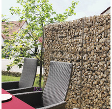 Gabionenwand aus Drahtkörben gefüllt mit Natursteinen als Sichtschutz im Garten neben Gartenstühlen aus Polyrattan.
