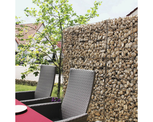 Gabionenwand aus Drahtkörben gefüllt mit Natursteinen als Sichtschutz im Garten neben Gartenstühlen aus Polyrattan.