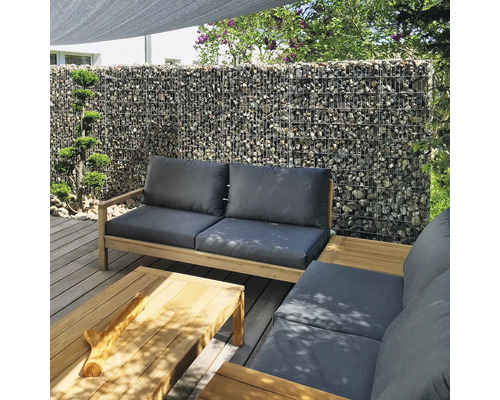 Moderne Gartenlounge auf Holzterrasse mit Gabionenwand im Hintergrund, Lounge-Möbel aus Holz mit grauen Auflagen und passendem Couchtisch.