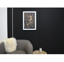 Décoration murale moderne avec des panneaux acoustiques noirs en lattes de bois dans un salon organisé avec un fauteuil gris et une table en bois.