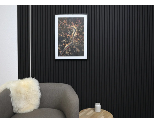 Décoration murale moderne avec des panneaux acoustiques noirs en lattes de bois dans un salon organisé avec un fauteuil gris et une table en bois.