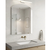 Salle de bain moderne lumineuse avec miroir mural arqué, robinetterie murale en aspect laiton, lavabo aspect béton et meuble sous-vasque en bois.