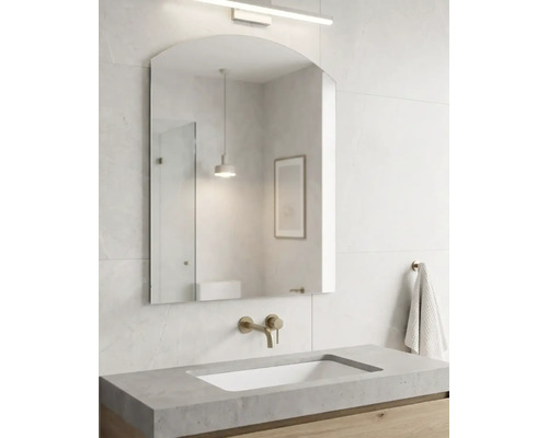 Helles, modernes Badezimmer mit gewölbtem Wandspiegel, Wandarmatur in Messingoptik, Waschtisch in Betonoptik und einem Unterschrank aus Holz.