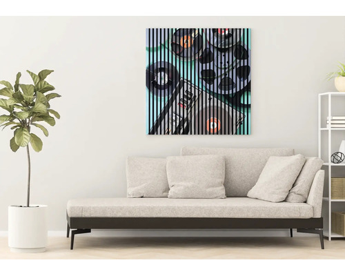 Salon moderne avec un canapé beige clair, une plante verte et un tableau carré représentant des bobines audio vintage avec des rayures noires.