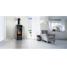 Moderner Kaminofen mit Steinverkleidung und brennendem Feuer in einem hellen, geräumigen Wohnzimmer mit Sessel und Stehlampe.