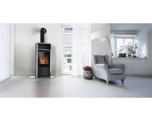 Moderner Kaminofen mit Steinverkleidung und brennendem Feuer in einem hellen, geräumigen Wohnzimmer mit Sessel und Stehlampe.
