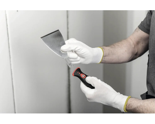 Couteau à enduire avec lame interchangeable et poignée ergonomique, tenu avec des gants de travail.