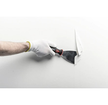 Main avec gant de travail utilisant un couteau à enduire pour retirer du papier peint d'un mur.