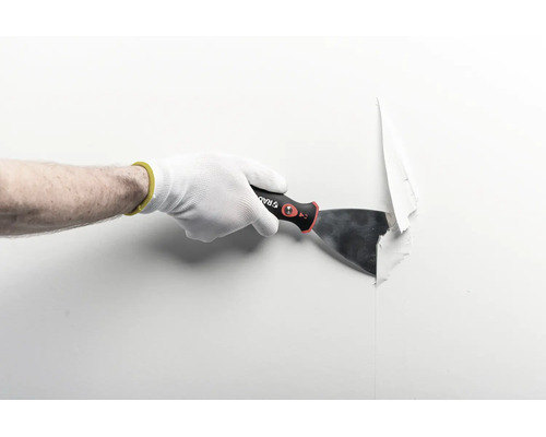 Main avec gant de travail utilisant un couteau à enduire pour retirer du papier peint d'un mur.