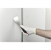Une main gantée utilise un couteau à enduire pour appliquer de l'enduit sur une plaque de plâtre.