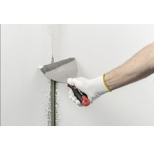 Main avec un couteau à enduire Rautner lissant de l'enduit sur un joint dans un mur.