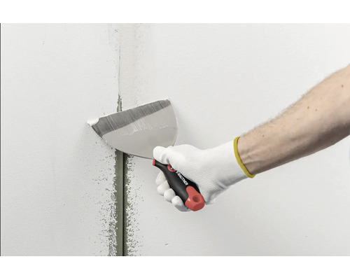 Main avec un couteau à enduire Rautner lissant de l'enduit sur un joint dans un mur.