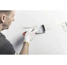 Une personne applique de l'enduit sur un mur à l'aide d'un couteau à enduire en métal.