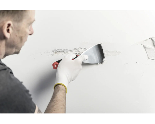 Une personne applique de l'enduit sur un mur à l'aide d'un couteau à enduire en métal.