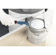 Personne ouvrant un pot de peinture avec un grattoir à peinture multifonction en métal sur un support en bois.