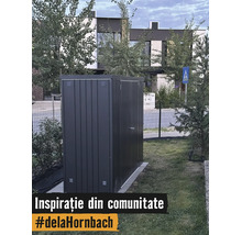 Abri de jardin moderne en métal gris foncé sur une pelouse dans un jardin devant une maison.