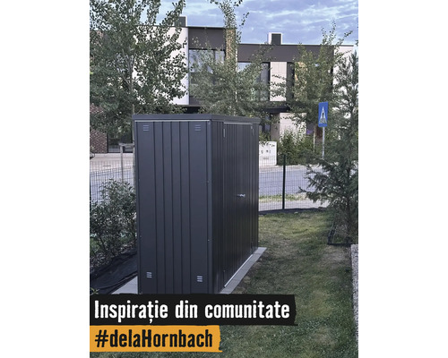 Abri de jardin moderne en métal gris foncé sur une pelouse dans un jardin devant une maison.