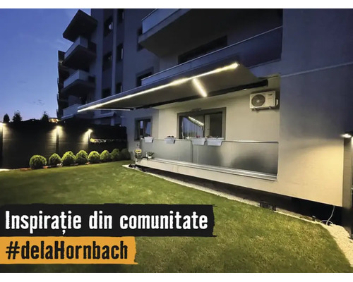 Store banne éclairé avec bandes LED intégrées au-dessus d'un balcon avec garde-corps en verre et pelouse entretenue la nuit.
