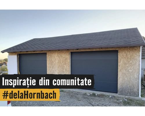Doppelgarage am Bau mat OSB-Plattenwänn, zwee antrazitfarwene Sektionaldieren an engem donkele Schindeldach.