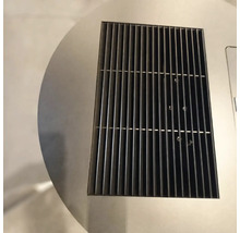 Gros plan d'une grille de ventilation rectangulaire en métal noir intégrée dans une surface circulaire en acier inoxydable.