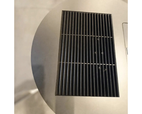 Gros plan d'une grille de ventilation rectangulaire en métal noir intégrée dans une surface circulaire en acier inoxydable.