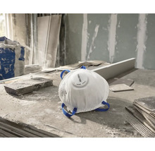 Masque de protection respiratoire Rautner blanc avec soupape d'expiration et sangles bleues sur un chantier poussiéreux.
