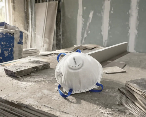 Masque de protection respiratoire Rautner blanc avec soupape d'expiration et sangles bleues sur un chantier poussiéreux.