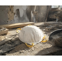 Masque de protection respiratoire blanc sur un établi poussiéreux dans un atelier avec des outils à bois et de la sciure.