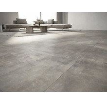 Salon moderne avec des carreaux de sol grand format aspect béton, un canapé gris et une table en bois.